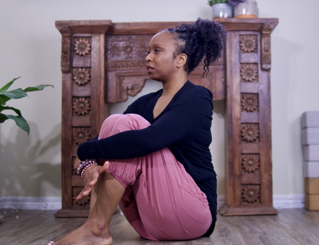 Kristeen is sitting on the floor with her hands around her legs and breathing.